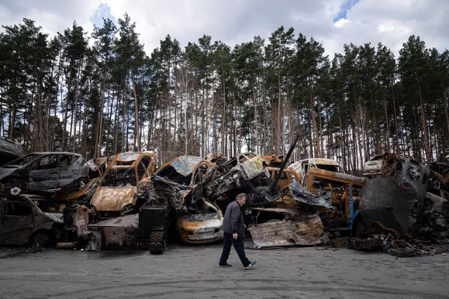 Một người đàn ông đi qua nơi để các phương tiện vũ trang và ô tô bị đốt cháy, ở ngoại ô Kiev.